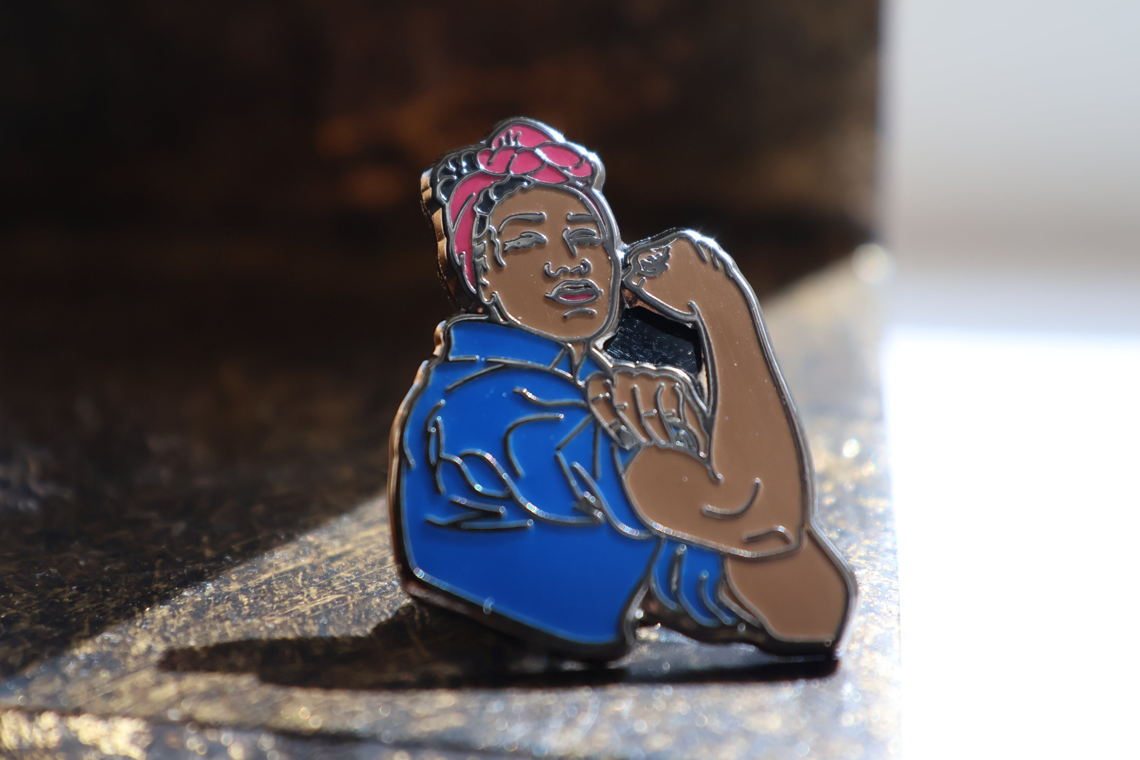 Pin with a stylized depiction of a black woman flexing her arm in the sunlight.
