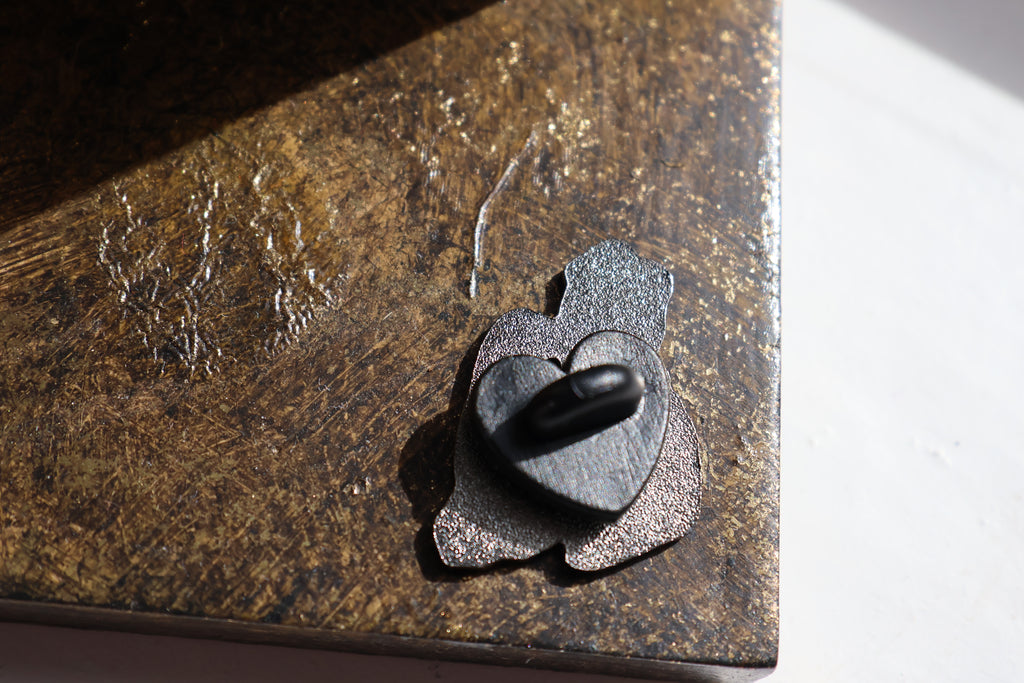 Image show the back of the pin which has a black heart shaped in back