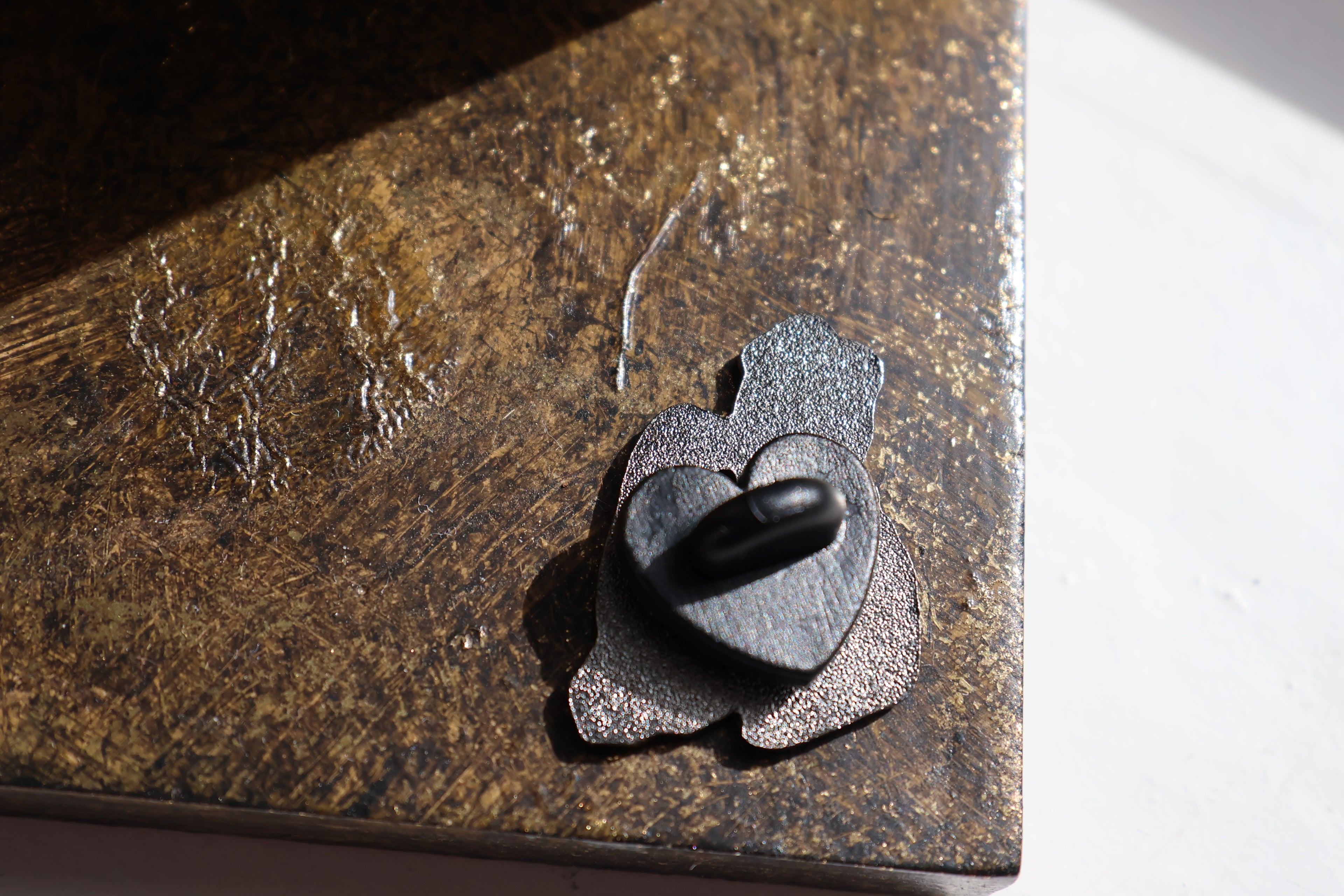 Image show the back of the pin which has a black heart shaped in back
