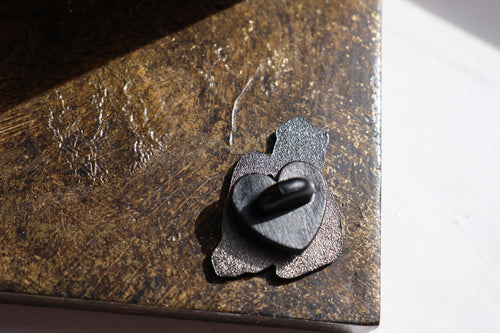 Image show the back of the pin which has a black heart shaped in back