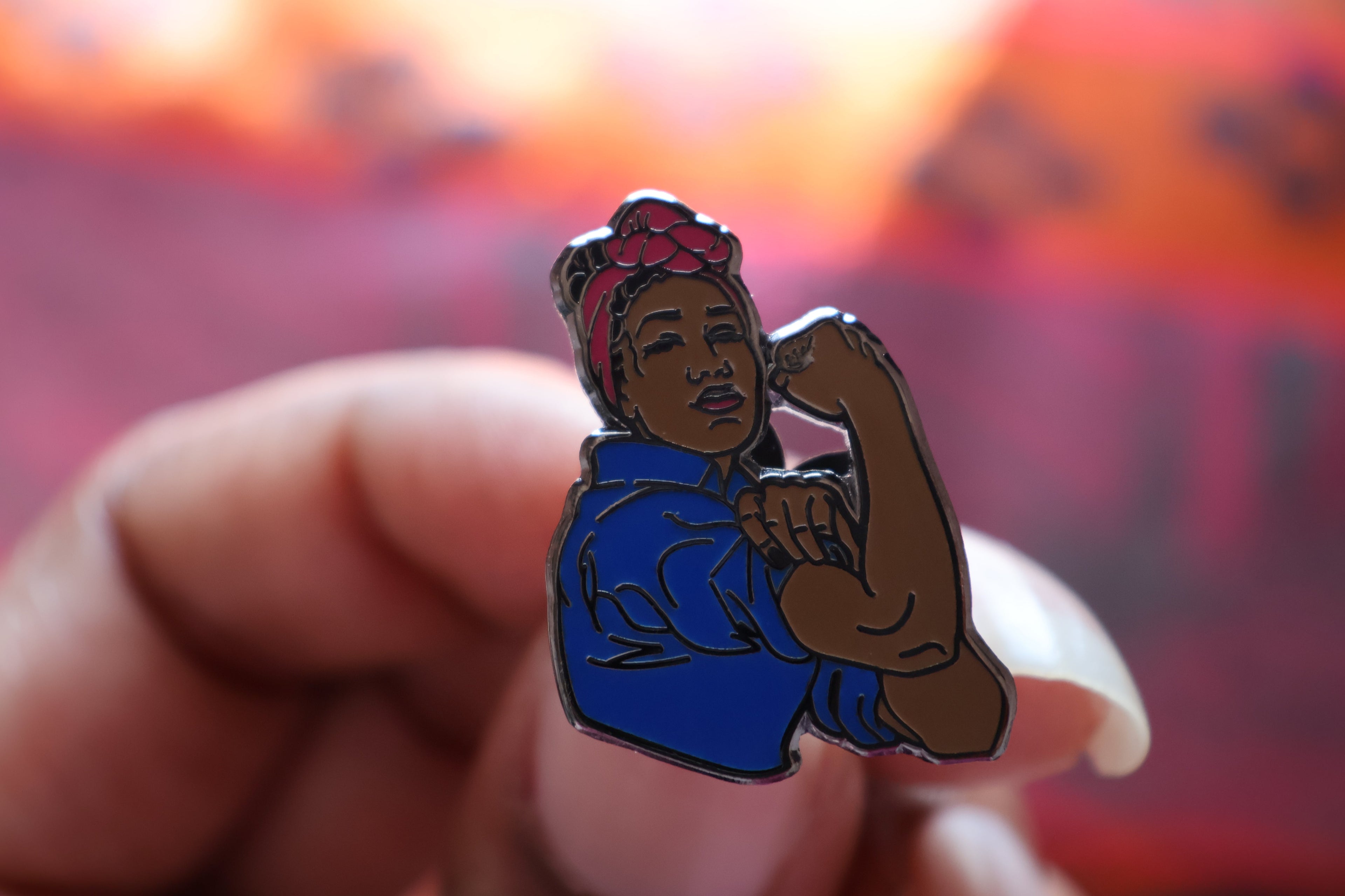 Pin with a stylized illustration of a black woman flexing her arm, held against a blurred background.